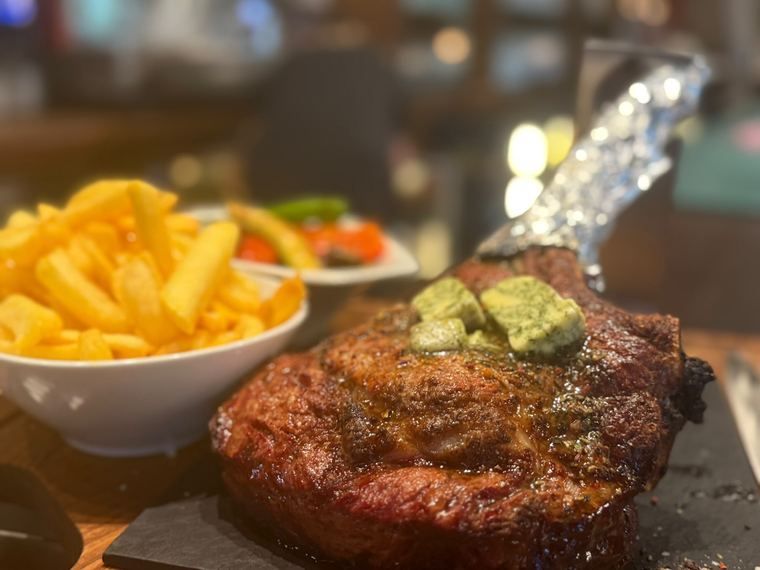 Tomahawk Steak mit Kräuterbutter und Pommes im Restaurant