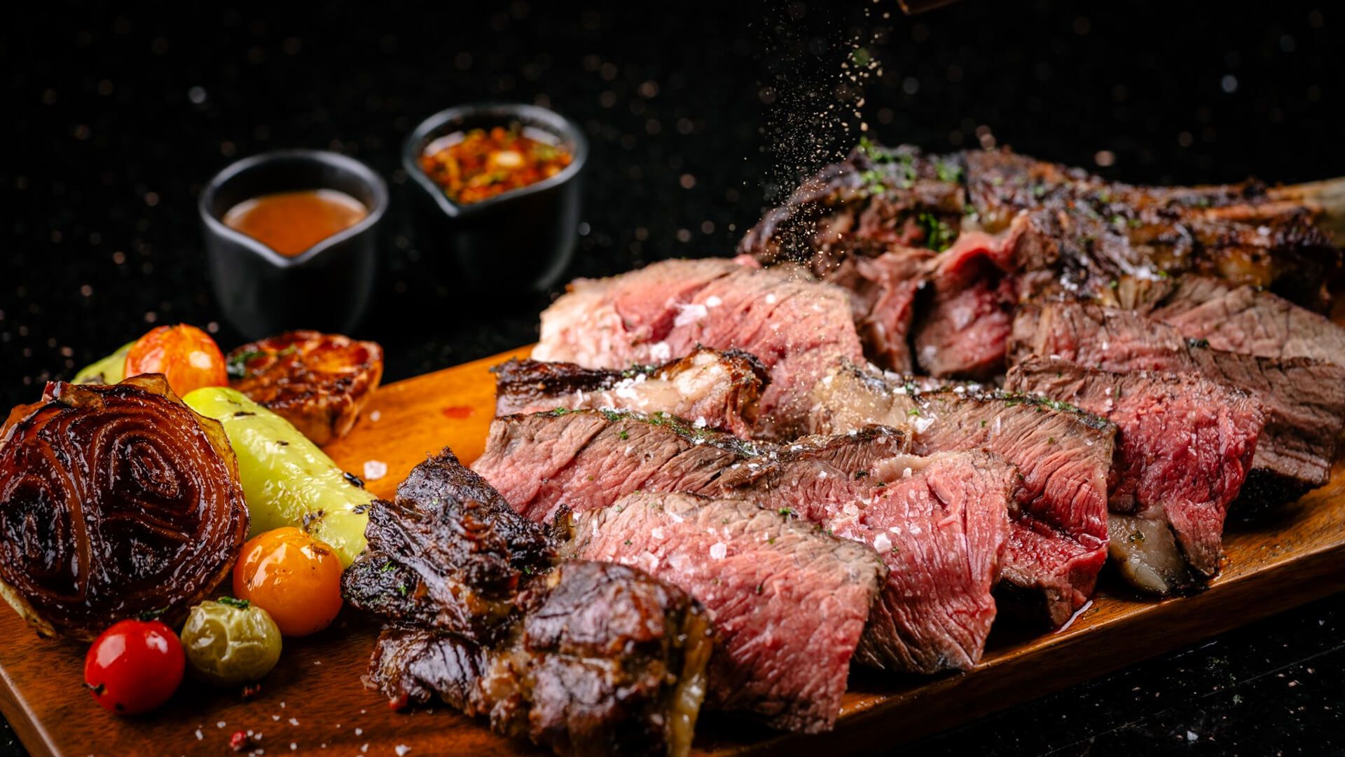 Aufgeschnittenes Steak mit Grillgemüse und Saucen auf dem Holzbrett
